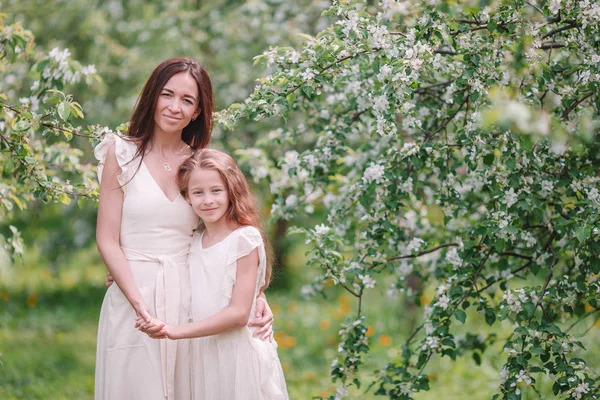 Urocza dziewczynka z młodą matką w kwitnącym wiśniowym ogrodzie w piękny wiosenny dzień — Zdjęcie stockowe