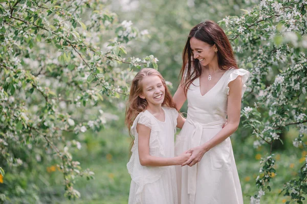 Adorable niña con madre joven en el floreciente jardín de cerezos en el hermoso día de primavera —  Fotos de Stock