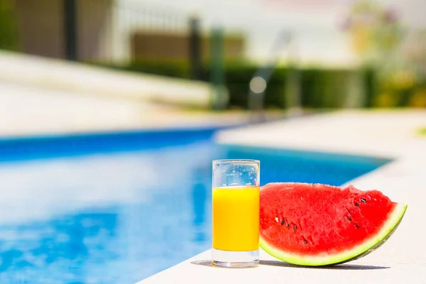 Summer and fresh theme: red ripe slice watermelon and glass of orange juice near pool — Stock Photo, Image