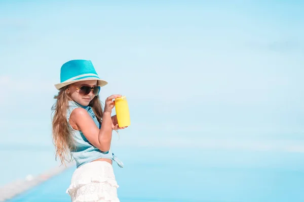 Liten flicka med flaska solkräm i poolen — Stockfoto