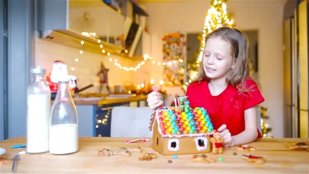 Little girls making Christmas gingerbread house at fireplace in decorated living room. — Stock Video