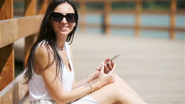 Χαριτωμένη γυναίκα διαβάζει το μήνυμα κειμένου στο κινητό τηλέφωνο, ενώ κάθεται στο πάρκο. — Αρχείο Βίντεο