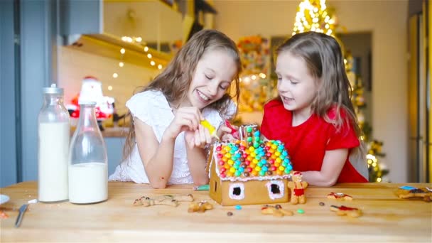 Little girls making Christmas gingerbread house at fireplace in decorated living room. — Stock Video