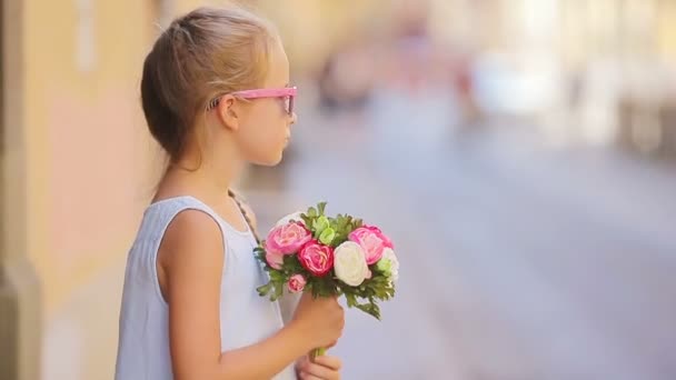 Adorable little girl with flowers bouquet walking in european city outdoors — Stock Video