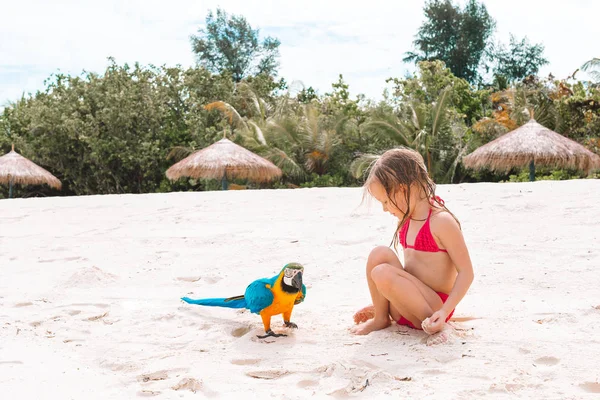 Adorable little girl at beach with colorful parrot — Stock Photo, Image