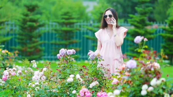 Chica joven en un jardín de flores entre hermosas rosas. Huele a rosas. — Vídeos de Stock