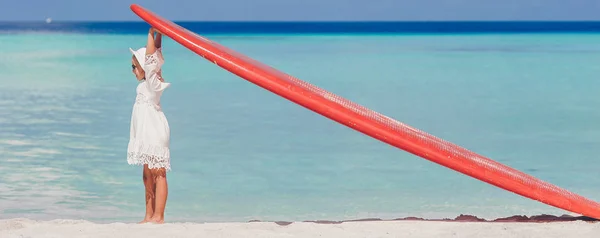Tropikal beyaz plaj üzerinde kırmızı büyük surfboard ile sevimli küçük kız — Stok fotoğraf