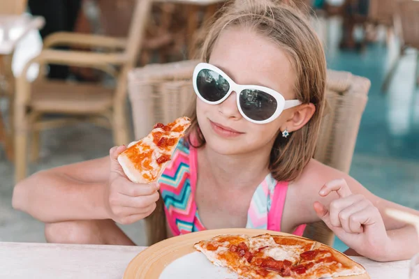 Retrato de una linda niña sentada junto a la mesa y comiendo pizza —  Fotos de Stock