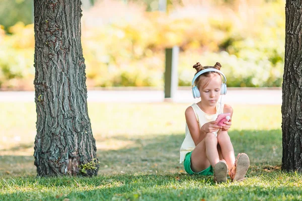 Liten bedårande flicka lyssnar musik i parken — Stockfoto