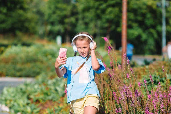 Liten bedårande flicka lyssnar musik i parken — Stockfoto