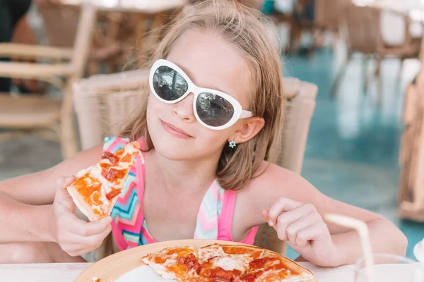 Retrato de una linda niña sentada junto a la mesa y comiendo pizza —  Fotos de Stock