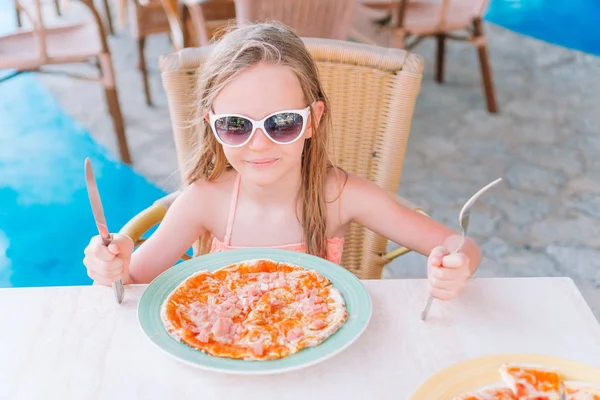 Retrato de una linda niña sentada junto a la mesa y comiendo pizza —  Fotos de Stock