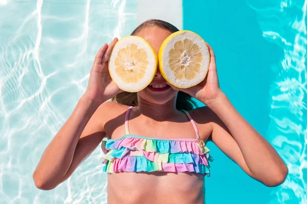 Little girl covering eyes with lemon halves near eyes on background swimming pool