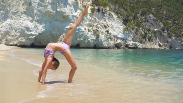 Menina ativa na praia se divertindo muito. Criança bonito fazendo exercícios esportivos na costa — Vídeo de Stock