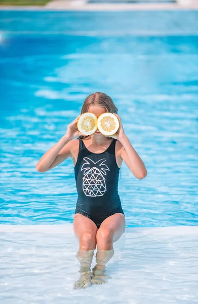 Menina cobrindo os olhos com metades de limão perto de olhos na piscina de fundo — Fotografia de Stock