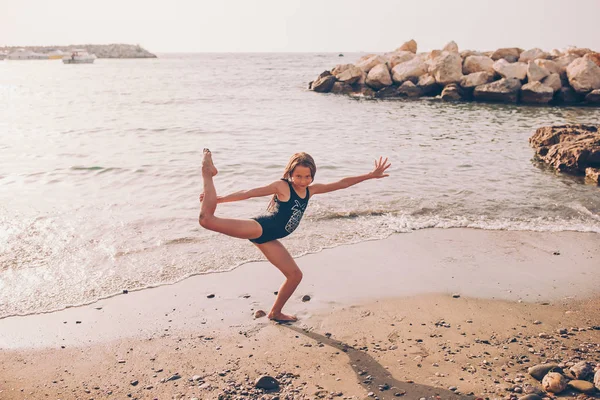 Active little girl at beach having a lot of fun. Cute kid making sporty exercises on the seashore — Stock Photo, Image