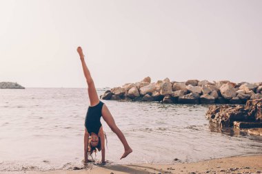 Sahilde hareketli küçük bir kız çok eğleniyor. Deniz kıyısında spor egzersizleri yapan tatlı çocuk.