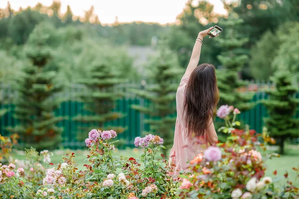 Chica joven en un jardín de flores entre hermosas rosas. Huele a rosas. —  Fotos de Stock