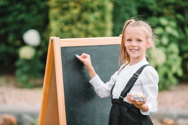 Happy little schoolgirl with a chalkboard outdoor — Stock Photo, Image