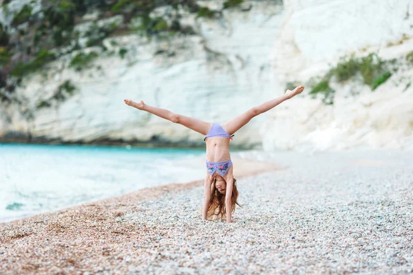 Active little girl at beach having a lot of fun. Cute kid making sporty exercises on the seashore — Stock Photo, Image