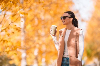 Sonbahar konsepti: Sonbahar parkında sonbahar yaprakları altında kahve içen güzel bir kadın.