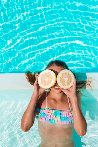 Niña cubriendo los ojos con mitades de limón cerca de los ojos en la piscina de fondo — Foto de Stock