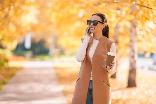 El concepto de otoño - la mujer hermosa que bebe café en el parque otoñal bajo el follaje otoñal — Foto de Stock