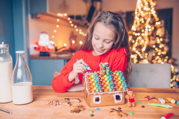 Meisjes maken kerst peperkoek huis bij open haard in ingerichte woonkamer. — Stockfoto