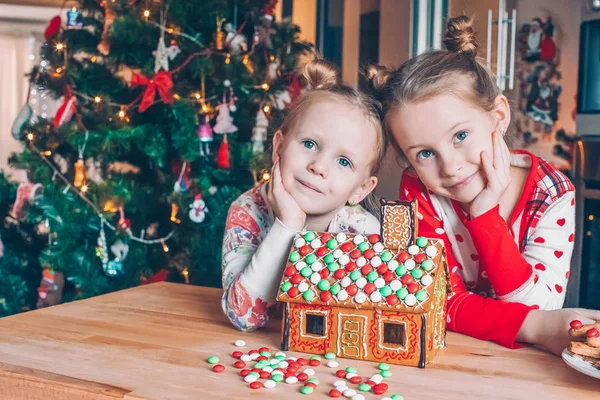 장식이 된 거실의 벽난로에서 크리스마스 진저브레드 집을 짓고 있는 소녀들. — 스톡 사진