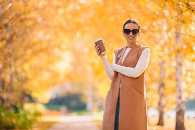 Sonbahar konsepti: Sonbahar parkında sonbahar yaprakları altında kahve içen güzel bir kadın.