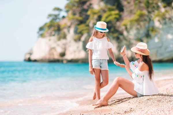 Mãe aplicando creme de proteção solar para sua filha na praia tropical — Fotografia de Stock