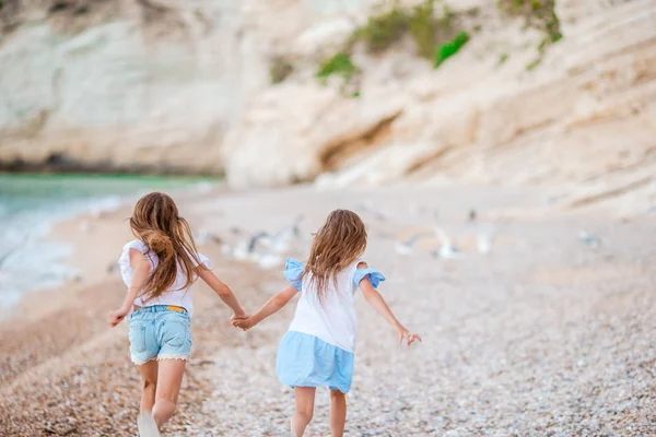 Little happy funny girls have a lot of fun at tropical beach playing together. Sunny day with rain in the sea — Stock Photo, Image