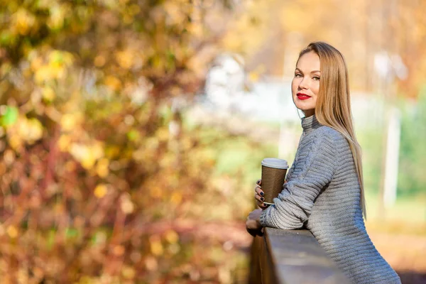 Jesienna koncepcja - piękna kobieta pijąca kawę w jesiennym parku pod jesiennymi liśćmi — Zdjęcie stockowe