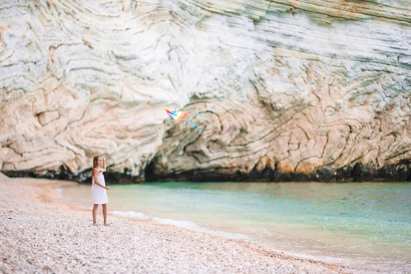 Kleines Mädchen fliegt einen Drachen am Strand mit türkisfarbenem Wasser — Stockfoto