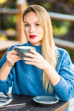 Sonbahar konsepti: Sonbahar parkında sonbahar yaprakları altında kahve içen güzel bir kadın.