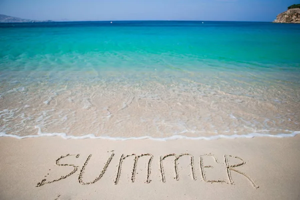 Palabra de verano escrito a mano en la playa de arena con ola suave del océano en el fondo —  Fotos de Stock