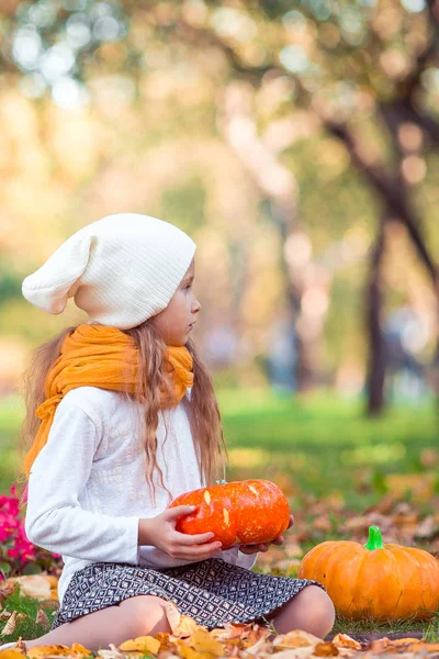 Μικρό αξιολάτρευτο κορίτσι με κολοκύθα σε εξωτερικούς χώρους σε μια ζεστή ημέρα του φθινοπώρου. — Φωτογραφία Αρχείου