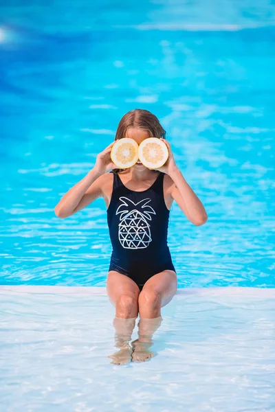 Ragazzina che copre gli occhi con mezze limone vicino agli occhi sullo sfondo piscina — Foto Stock