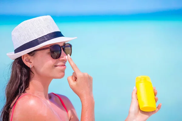 Ung lycklig kvinna som applicerar solkräm på näsan på vit strand — Stockfoto