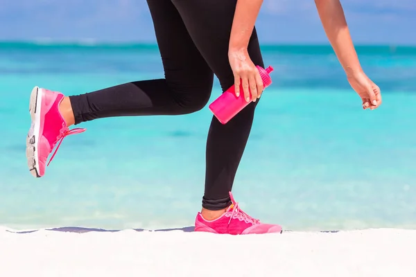 Närbild av kvinnliga ben i sneakers körs på vit sandstrand — Stockfoto