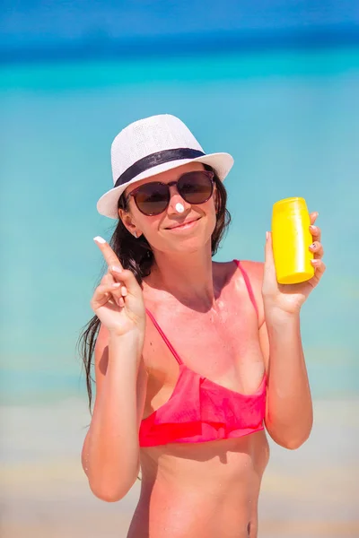 Young happy woman applying suntan lotion on her nose on white beach — Stock Photo, Image