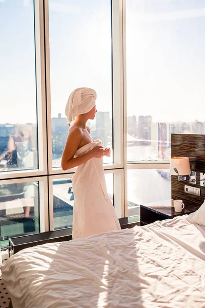 Hermosa mujer joven en toalla de baño blanca en la cabeza relajante después de la ducha en la cama con taza de café —  Fotos de Stock