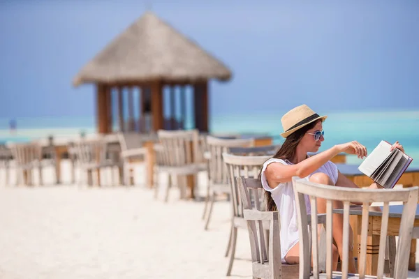 Młoda kobieta czytając na zewnątrz kawiarnia na plaży — Zdjęcie stockowe