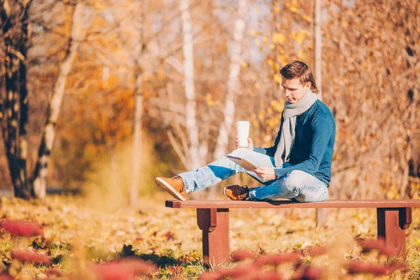 Młody człowiek pijący kawę z telefonem w jesiennym parku na świeżym powietrzu — Zdjęcie stockowe