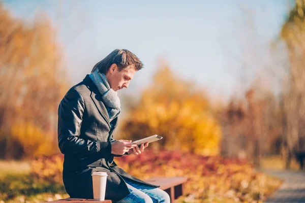 Young man drinking coffee with phone in autumn park outdoors — Stock Photo, Image