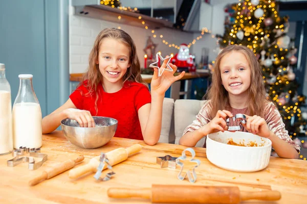 Meisjes maken kerst peperkoek huis bij open haard in ingerichte woonkamer. — Stockfoto