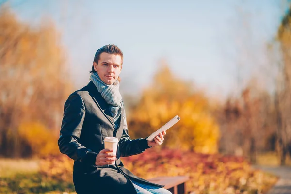 3.在秋日的公园里，一个年轻人正在户外用手机喝咖啡 — 图库照片
