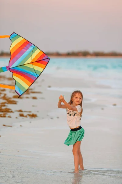 Kleines Mädchen mit fliegendem Drachen am tropischen Strand. Kinder spielen am Meeresufer. — Stockfoto