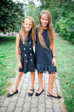 Okullarının önünde poz veren gülümseyen iki küçük kız..