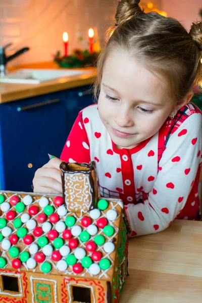 Klein meisje maakt kerst peperkoek huis bij open haard in ingerichte woonkamer. — Stockfoto